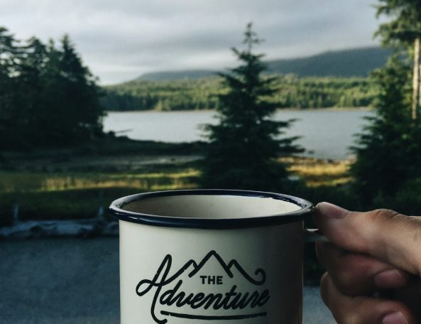 Taza con la palabra "Adventure" frente a un lago y montañas al fondo.