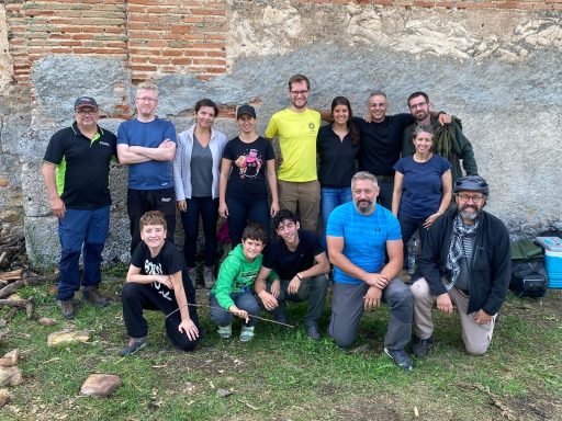 International Team Building Grupo de personas sonrientes posando frente a una pared de piedra y ladrillo.