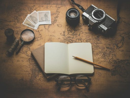 Mapa antiguo, cámara, gafas, lupa y cuaderno con lápiz sobre una mesa de madera.