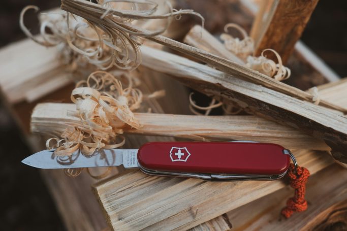 Cuchillo suizo rojo sobre troncos de madera y astillas.