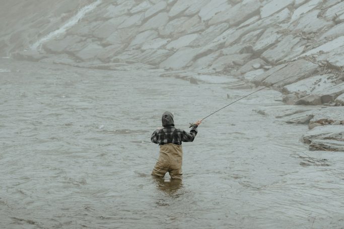 Hombre pescando en un río, de pie en el agua con caña de pescar.